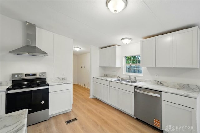 665 Diamond Loop, Middletown, OH 45044 - kitchen with appliances with stainless steel finishes, wall chimney range hood, a sink, white cabinetry, and light wood-style floors