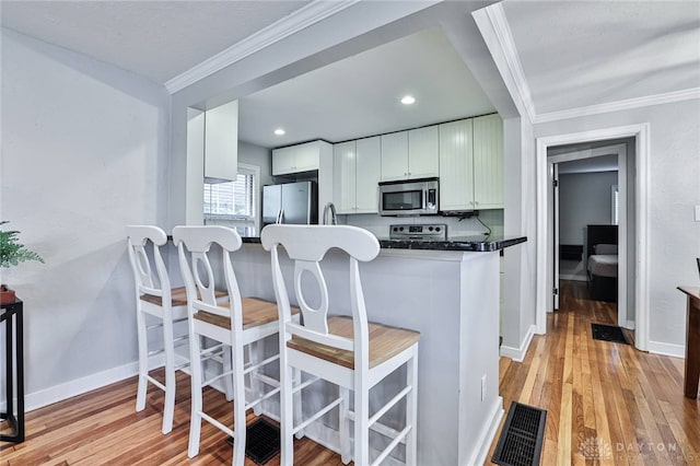 407 Claranna Ave, Oakwood, OH 45419 - kitchen with appliances with stainless steel finishes, light wood finished floors, a kitchen breakfast bar, crown molding, and white cabinets
