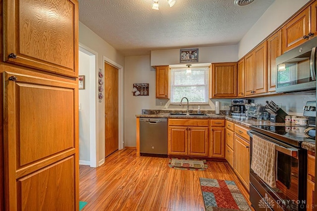 286 Chamberlin Dr, Hamilton, OH 45013 - kitchen featuring appliances with stainless steel finishes, a sink, light wood-style flooring, brown cabinets, and a textured ceiling