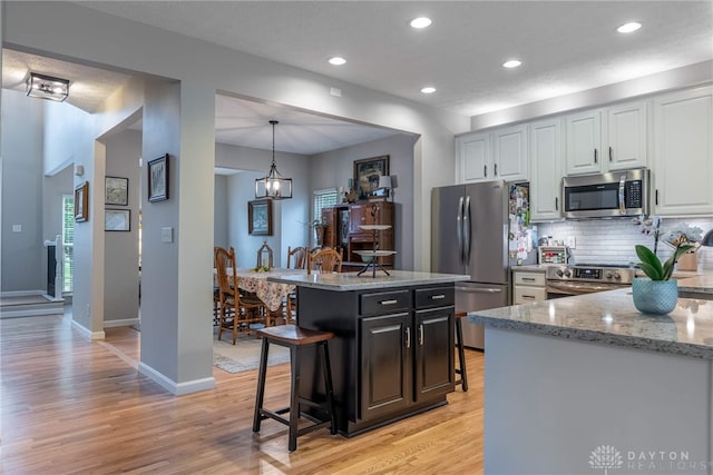 989 Brooke Ln, Xenia, OH 45385 - kitchen with appliances with stainless steel finishes, a kitchen bar, decorative backsplash, light wood-style flooring, and light stone countertops
