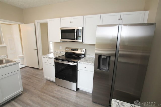 1716 Xenia Ave, Dayton, OH 45410 - kitchen featuring appliances with stainless steel finishes, white cabinets, light wood-style flooring, light stone countertops, and a textured ceiling