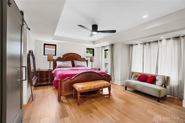 1000 Paradrome St, Cincinnati, OH 45202 - bedroom with a barn door, light wood-style flooring, a tray ceiling, a ceiling fan, and recessed lighting