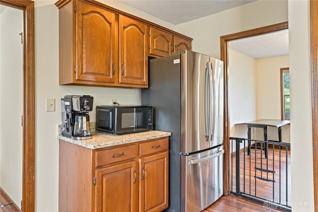 1747 Maple Ln, Beavercreek, OH 45432 - kitchen with freestanding refrigerator, black microwave, brown cabinetry, light stone counters, and wood finished floors