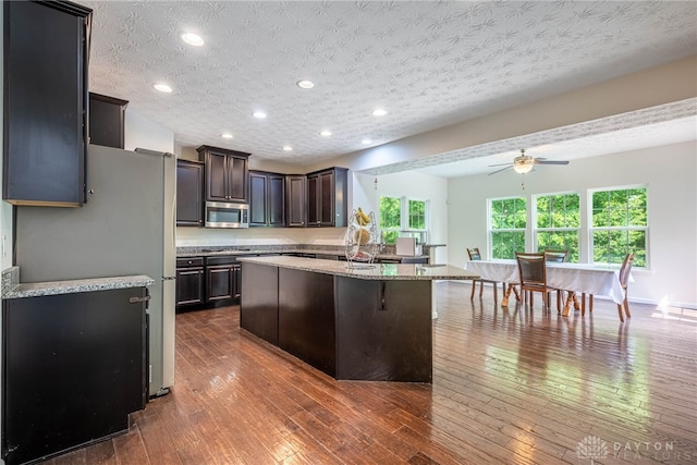 8730 Dowd Ct, Washington Twp, OH 45458 - kitchen with stainless steel appliances, ceiling fan, dark brown cabinetry, a center island with sink, and light stone counters