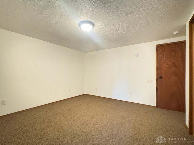 5565 Short Rd, New Carlisle, OH 45344 - unfurnished room featuring a textured ceiling, dark colored carpet, and a smoke detector
