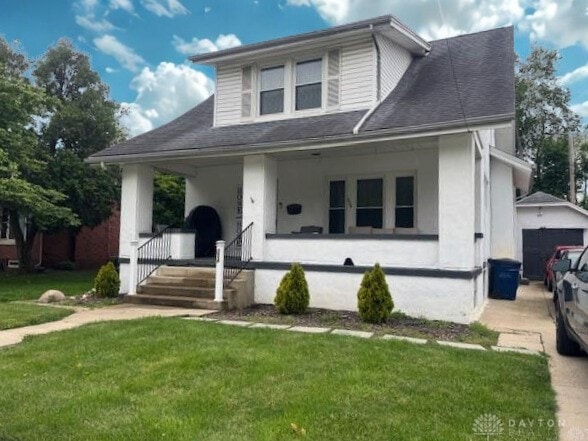 224 S Wolf Creek St, Brookville, OH 45309 - bungalow featuring covered porch, a front lawn, a shingled roof, and stucco siding