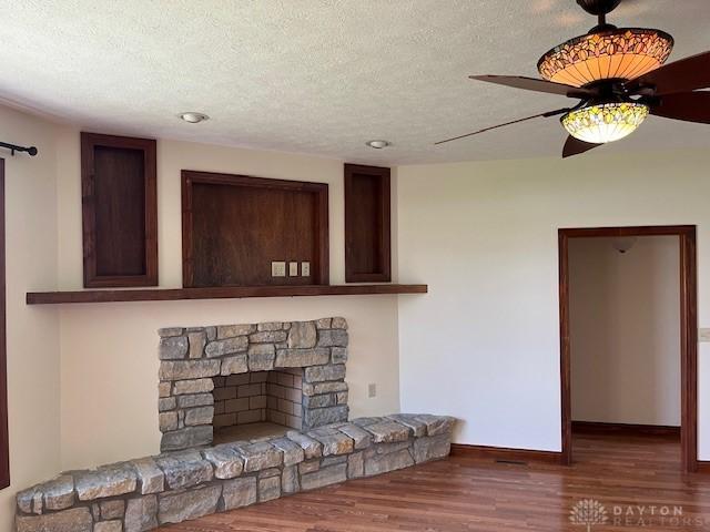 5671 Sonora Rd, Lewisburg, OH 45338 - unfurnished living room featuring wood finished floors, a textured ceiling, a ceiling fan, baseboards, and a stone fireplace