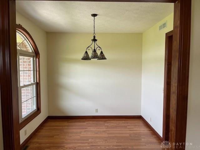 5671 Sonora Rd, Lewisburg, OH 45338 - empty room featuring wood finished floors, baseboards, a textured ceiling, and a chandelier