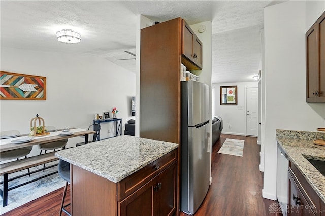 9675 Pellston Way, Miamisburg, OH 45342 - kitchen featuring freestanding refrigerator, a textured ceiling, dark wood-style floors, a breakfast bar area, and light stone counters