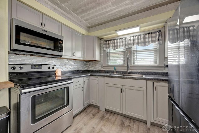 4975 Hamilton Eaton Rd, Hamilton, OH 45013 - kitchen featuring stainless steel appliances, a sink, dark countertops, backsplash, and light wood-type flooring