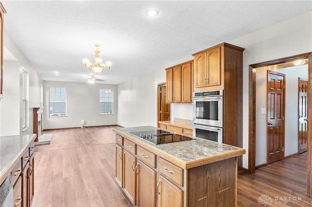 2159 Bassett Ct, Beavercreek, OH 45434 - kitchen featuring double oven, black electric cooktop, a chandelier, a kitchen island, and wood finished floors