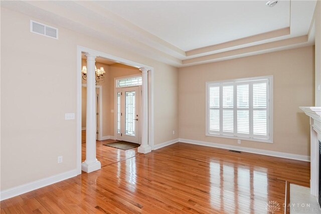 2082 Tamarack Ridge Ct, Beavercreek, OH 45431 - unfurnished living room with ornate columns, light wood finished floors, a chandelier, a tray ceiling, and a high end fireplace