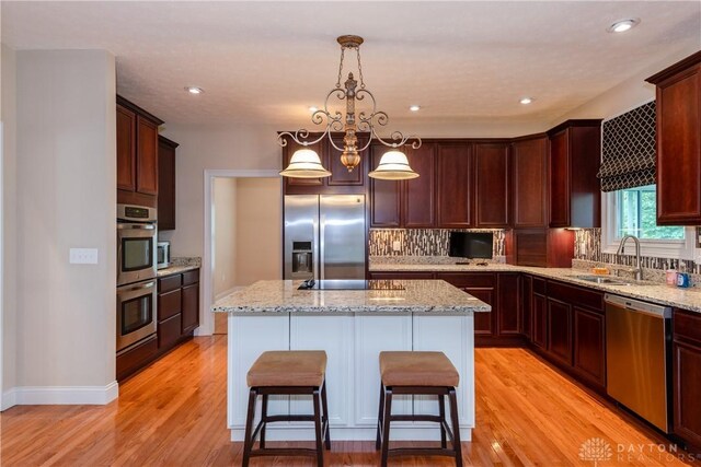 2082 Tamarack Ridge Ct, Beavercreek, OH 45431 - kitchen with appliances with stainless steel finishes, light wood-style floors, backsplash, a center island, and a breakfast bar area