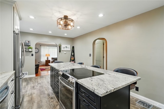 646 Barnhart Rd, Troy, OH 45373 - kitchen featuring arched walkways, appliances with stainless steel finishes, dark cabinets, a center island, and light wood-style floors