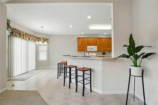 3862 Robinson Vail Rd, Franklin, OH 45005 - kitchen with white microwave, a breakfast bar, a chandelier, brown cabinetry, and recessed lighting