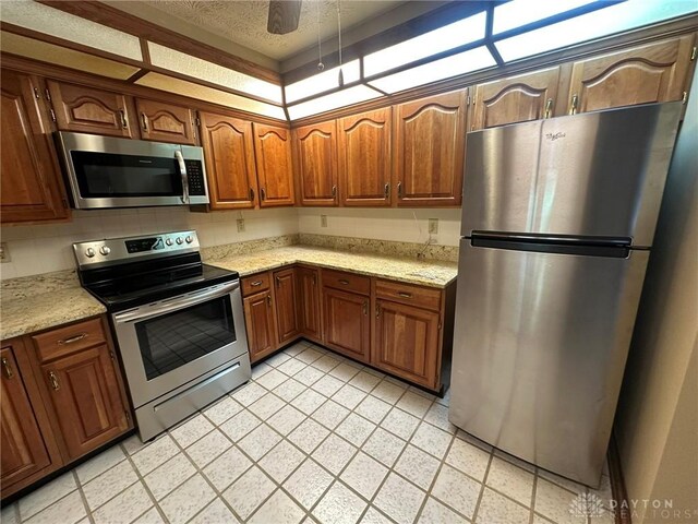 6553 Stillcrest Way, Dayton, OH 45414 - kitchen featuring appliances with stainless steel finishes, a textured ceiling, light stone counters, and brown cabinets