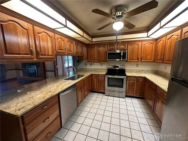 6553 Stillcrest Way, Dayton, OH 45414 - kitchen with stainless steel appliances, light stone counters, brown cabinetry, a ceiling fan, and a brick fireplace