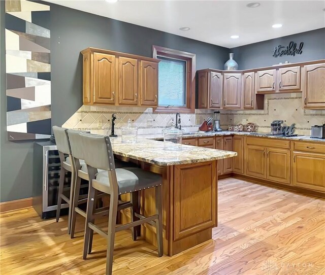 7171 Dominican Dr, Clayton, OH 45415 - kitchen with a peninsula, light wood-style floors, a breakfast bar, light stone counters, and decorative backsplash