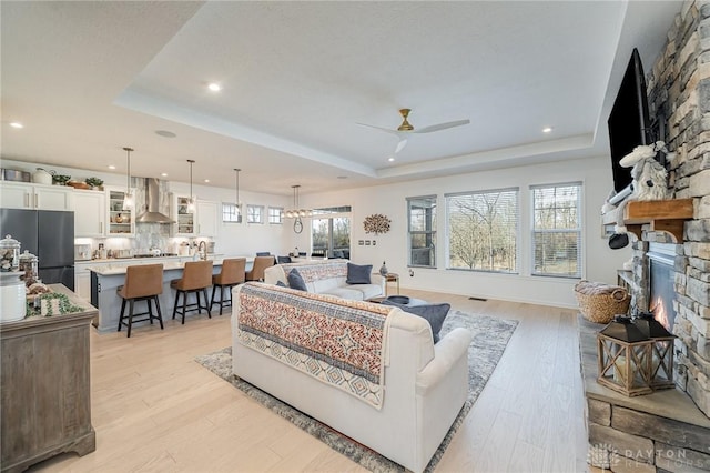 5078 Magellan Way, Franklin, OH 45005 - living area featuring a stone fireplace, a raised ceiling, ceiling fan, light wood-style floors, and recessed lighting