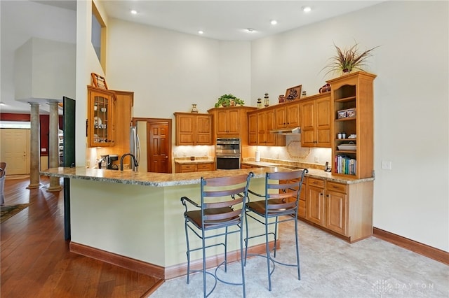 1106 Roger Scott Dr, Bellbrook, OH 45305 - kitchen featuring a high ceiling, appliances with stainless steel finishes, a peninsula, a breakfast bar, and brown cabinets