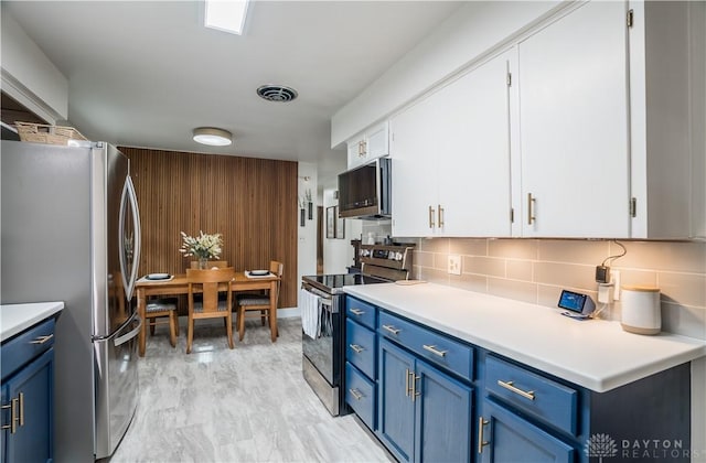 2435 S County Road 25a, Troy, OH 45373 - kitchen featuring stainless steel appliances, blue cabinets, white cabinetry, decorative backsplash, and wooden walls