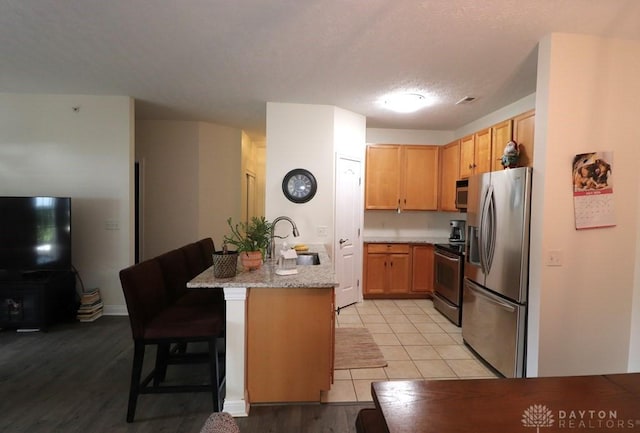 3224 Grand Falls Blvd, Maineville, OH 45039 - kitchen with stainless steel appliances, a kitchen bar, light wood-type flooring, light stone countertops, and a peninsula