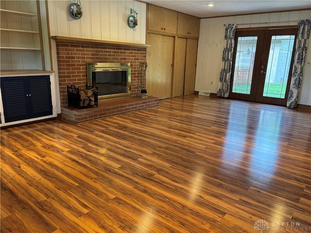 215 W Martindale Rd, Englewood, OH 45322 - unfurnished living room featuring wood finished floors, french doors, built in shelves, wood walls, and a brick fireplace