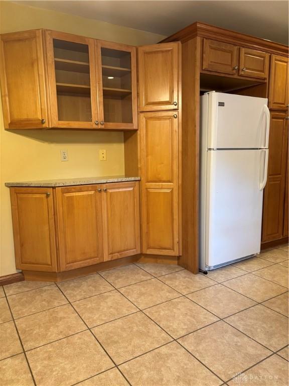 215 W Martindale Rd, Englewood, OH 45322 - kitchen with freestanding refrigerator, light tile patterned floors, glass insert cabinets, and brown cabinetry