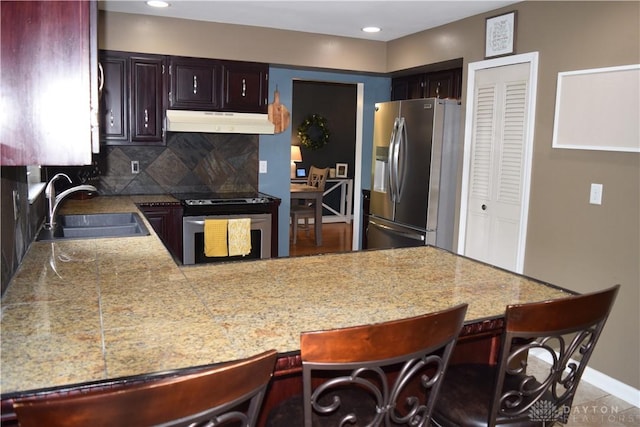 5468 Split Rock Dr, Dayton, OH 45424 - kitchen with appliances with stainless steel finishes, under cabinet range hood, a peninsula, decorative backsplash, and a breakfast bar