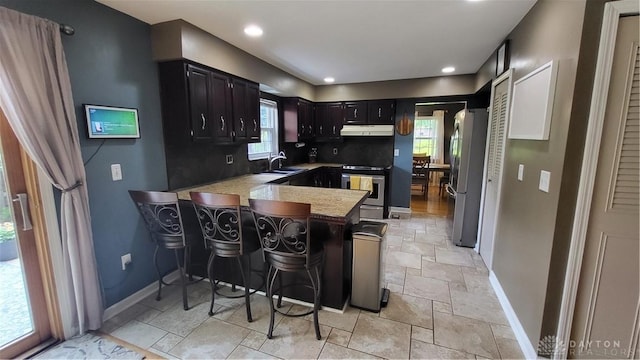 5468 Split Rock Dr, Dayton, OH 45424 - kitchen featuring appliances with stainless steel finishes, under cabinet range hood, a peninsula, stone tile flooring, and a breakfast bar area