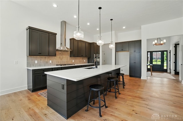 8559 Wandering Brook Way, Waynesville, OH 45068 - kitchen featuring wall chimney exhaust hood, stainless steel gas stovetop, backsplash, a large island with sink, and light wood-type flooring