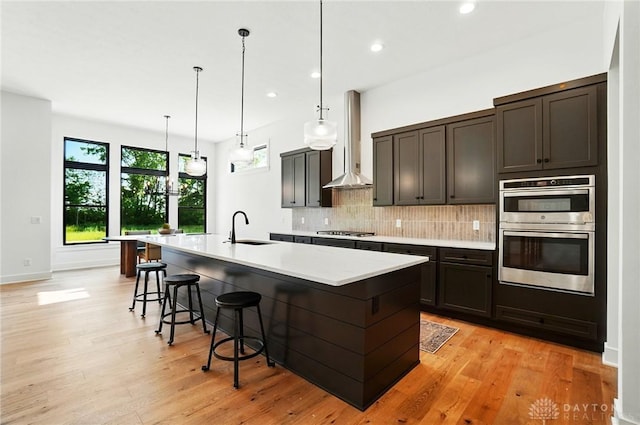 8559 Wandering Brook Way, Waynesville, OH 45068 - kitchen with stainless steel appliances, wall chimney range hood, decorative backsplash, light countertops, and a center island with sink