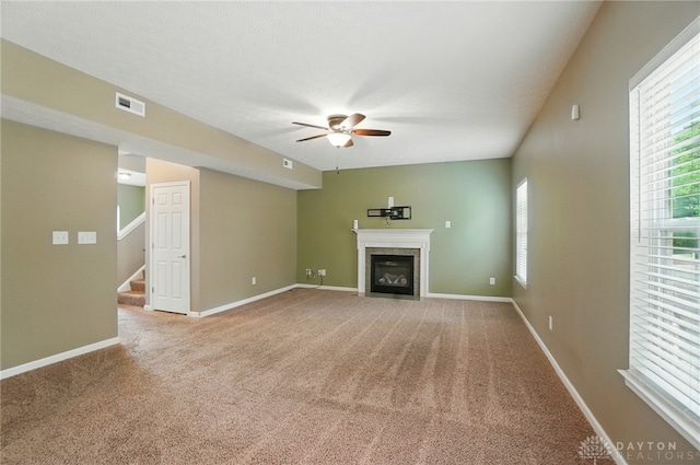 1956 Daffodil Dr, Xenia, OH 45385 - unfurnished living room featuring ceiling fan, a fireplace with flush hearth, carpet flooring, and stairway
