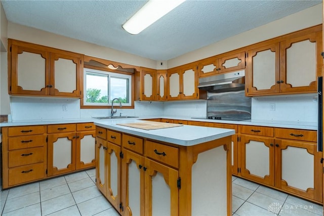 3372 Home Acres Ave, Beavercreek, OH 45431 - kitchen featuring light countertops, under cabinet range hood, light tile patterned flooring, a center island, and brown cabinets
