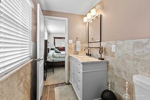 6814 Rushleigh Rd, Englewood, OH 45322 - bathroom featuring tile walls, wood finished floors, vanity, ensuite bathroom, and a wainscoted wall