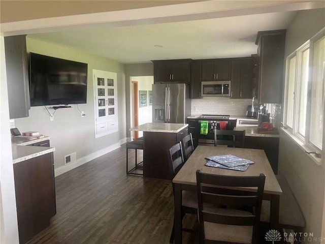 311 Swailes Rd, Troy, OH 45373 - kitchen with stainless steel appliances, decorative backsplash, dark wood-type flooring, a kitchen island, and light stone counters