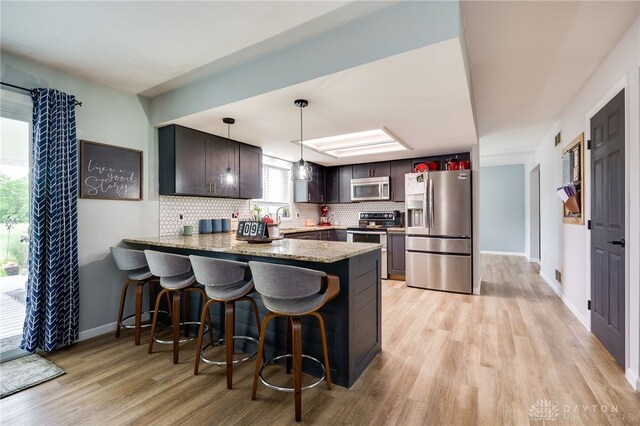 8282 Hile Ln, Germantown, OH 45327 - kitchen with stainless steel appliances, a peninsula, tasteful backsplash, light wood-style floors, and a kitchen breakfast bar