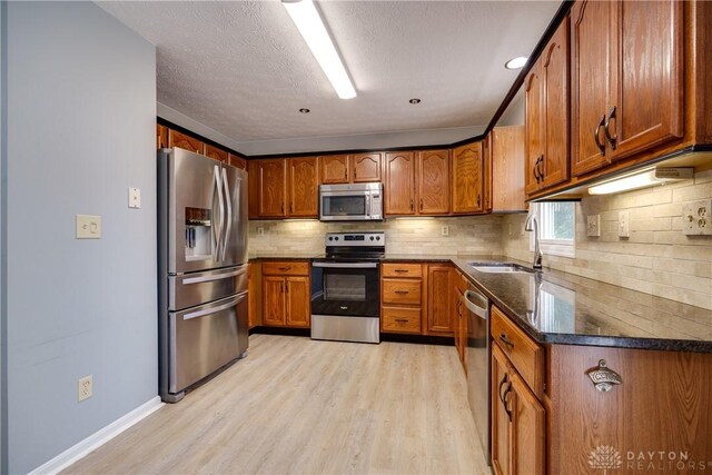 1360 Adamsmoor Dr, Waynesville, OH 45068 - kitchen with appliances with stainless steel finishes, light wood-type flooring, brown cabinetry, backsplash, and a textured ceiling