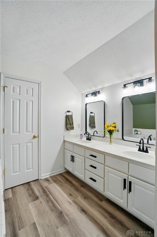 1510 Ash Ridge Ct, Vandalia, OH 45377 - bathroom featuring double vanity, vaulted ceiling, a textured ceiling, and wood finished floors