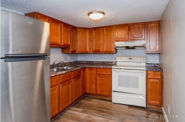 7293 Ellenridge Dr, Franklin, OH 45005 - kitchen with freestanding refrigerator, white electric range, under cabinet range hood, a textured ceiling, and brown cabinetry