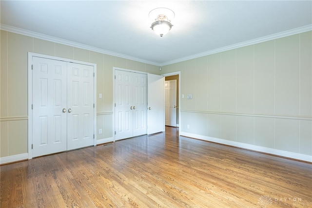 1919 Tait Circle Rd, Kettering, OH 45429 - unfurnished bedroom with wood finished floors, multiple closets, crown molding, and a decorative wall