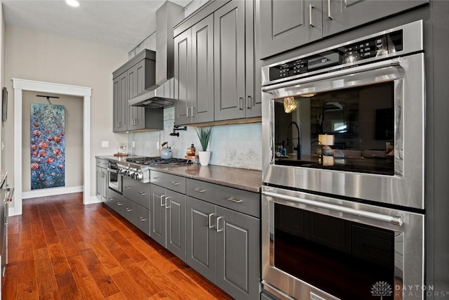 79 White Beech Ct, Springboro, OH 45066 - kitchen featuring appliances with stainless steel finishes, gray cabinetry, wall chimney range hood, dark wood-style floors, and dark countertops
