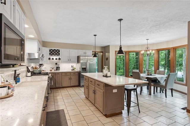 923 Lewis Creek Ct, Xenia, OH 45385 - kitchen featuring appliances with stainless steel finishes, ventilation hood, a breakfast bar, hanging light fixtures, and a chandelier