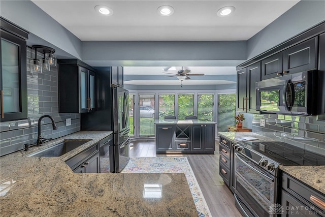 195 Sycamore Creek Dr, Springboro, OH 45066 - kitchen featuring appliances with stainless steel finishes, light stone countertops, a ceiling fan, decorative backsplash, and light wood-type flooring