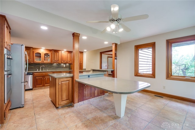 4911 Arabian Dr, Fairborn, OH 45324 - kitchen featuring a kitchen island, ornate columns, brown cabinetry, decorative backsplash, and a ceiling fan