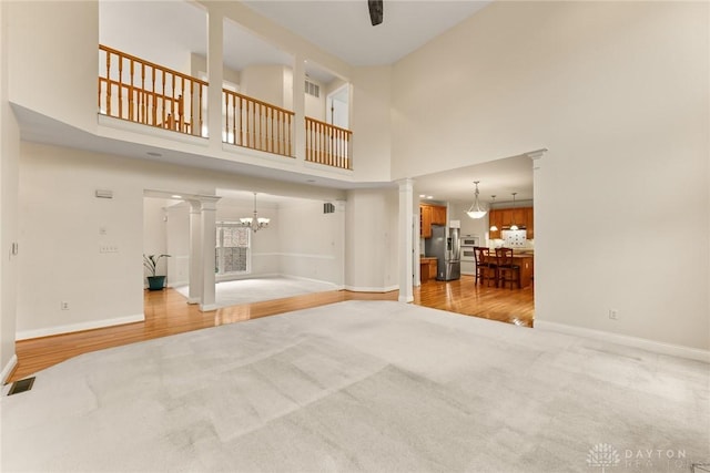 9764 Olde Georgetown Way, Dayton, OH 45458 - unfurnished living room featuring decorative columns, light colored carpet, a chandelier, a high ceiling, and light wood-style floors
