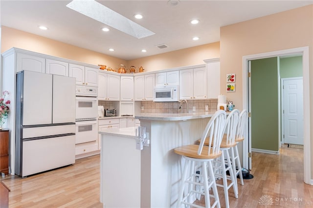866 Deer Run Rd, Centerville, OH 45459 - kitchen featuring white appliances, a skylight, white cabinets, light wood-style floors, and a peninsula