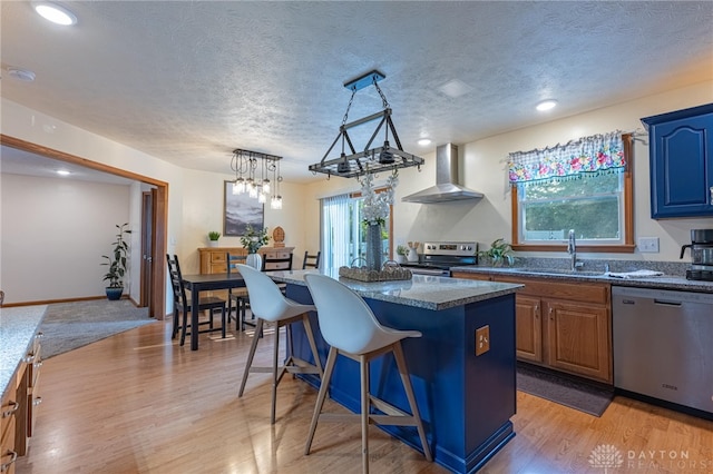 2610 Yorktown Ct, Beavercreek, OH 45434 - kitchen featuring appliances with stainless steel finishes, wall chimney range hood, a kitchen island, light wood finished floors, and a textured ceiling