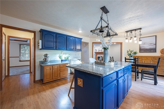 2610 Yorktown Ct, Beavercreek, OH 45434 - kitchen featuring blue cabinets, a textured ceiling, light wood-type flooring, a kitchen island, and a fireplace