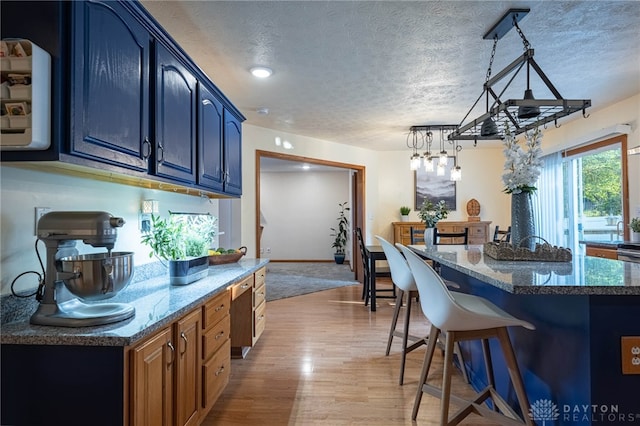 2610 Yorktown Ct, Beavercreek, OH 45434 - kitchen featuring a kitchen breakfast bar, light wood-type flooring, dark stone counters, a kitchen island, and a textured ceiling